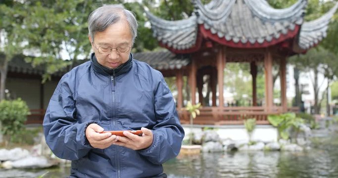 Asian senior man watching on cellphone in chinese garden