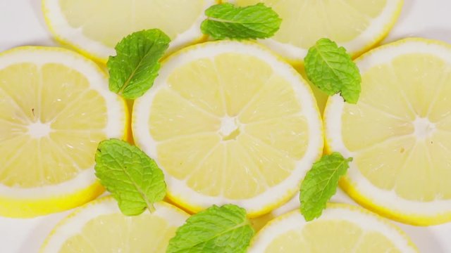 High angle view of slices of fresh lemon fruits and peppermint leaves, spinning on the table in the studio