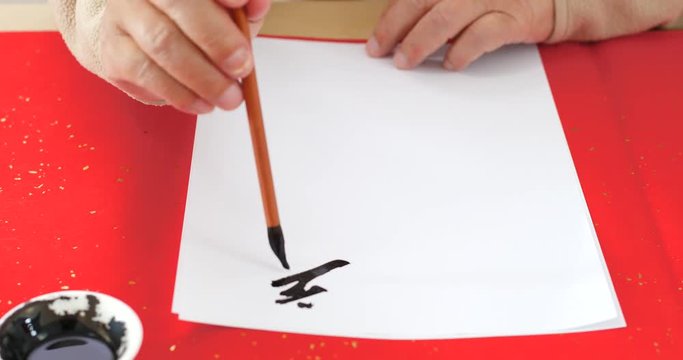 Patrice on wiring Chinese calligraphy on white paper for lunar new year, phrase meaning happy new year and wish you good fortune and may all your wishes come true