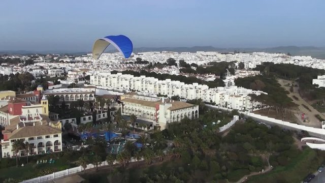 A man flying Paragliding with motor over the sea and little town at sunset