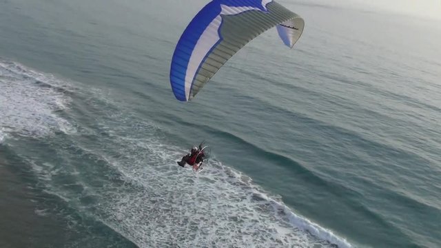 A man flying Paragliding with motor over the sea and little town at sunset
