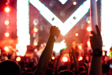 Crowd of hands up concert stage lights and people fan audience silhouette raising hands glow stick holding in the music festival rear view with spotlight glowing effect