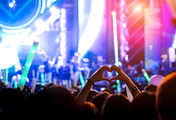 Hand gesture loves finger concert stage lights crowd or audience artist band in the music festival rear view with spotlights glowiing effect and people fan audience silhouette make heart shaped 