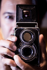 Man with old vintage camera in hands. Focus to man eyes. Vintage stylized photo of man photographer with old TLR (Twin Lens Reflex) Camera, ring-flash shot..