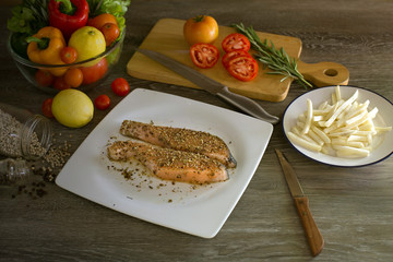 Prepare grill salmon with pepper and salt in white dish and ingredient in kitchen which has dim light