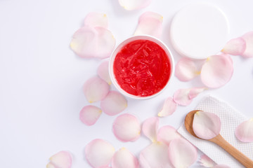 Spa accessories in Pink. Top view of body cream and pink rose flower petals on white background.