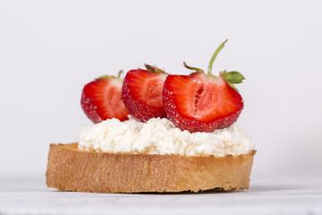 Sandwich from red strawberry, white cottage cheese and bread on the white wooden table, close up