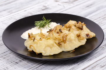 Ukrainian and Russian dishes - vareniki or dumplings with mashed potatoes or cottage cheese, fried onions and sour cream on wooden background