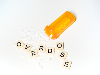 Tan tiles with black capital letters spelling Overdose with an open prescription bottle with white...