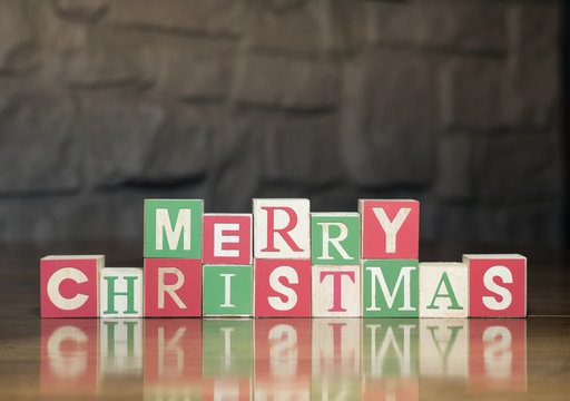 Wooden toy blocks with capital letters spelling Merry Christmas against a rock wall.