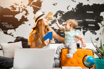 Happy and playful woman with baby boy sitting at the travel agency office with beautiful map on the...