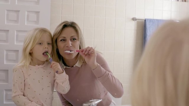 Mother and daughter at home brushing teeth in mirror