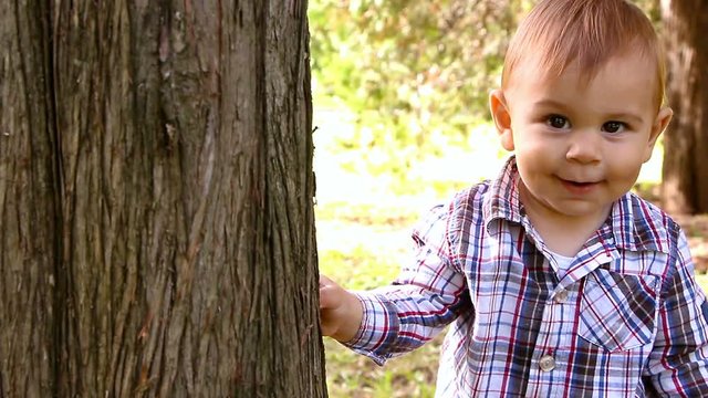 Portrait of caucasian one year old cute boy making his first steps, peaking out of a tree