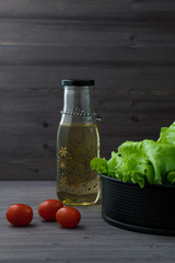 lettuce leaves in a bowl, a bottle and cherry tomatoes on a dark wooden background