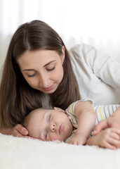 Beautiful mother looks at her 7 months old baby sleeping in the bed