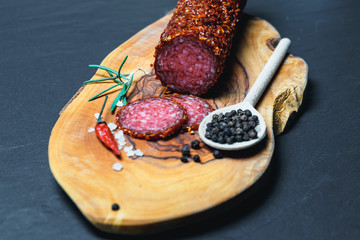 Dried salami crusted in ground red pepper on dark background