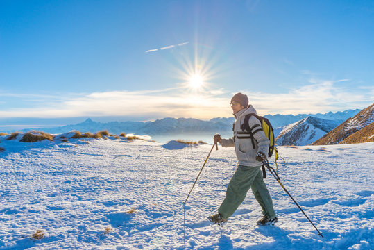 Woman backpacker trekking on snow on the Alps. Rear view, winter lifestyle, cold feeling, sun star in backlight, hiking poles.