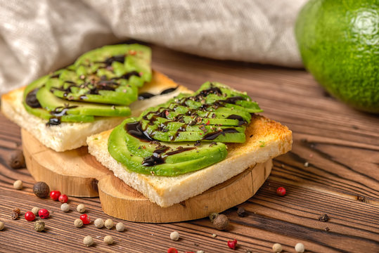 sandwiches with sliced avocado, white bread toast decorated alligator pear fruit, drizzled with sauce and sprinkle with pepper on wooden background, healthy eating