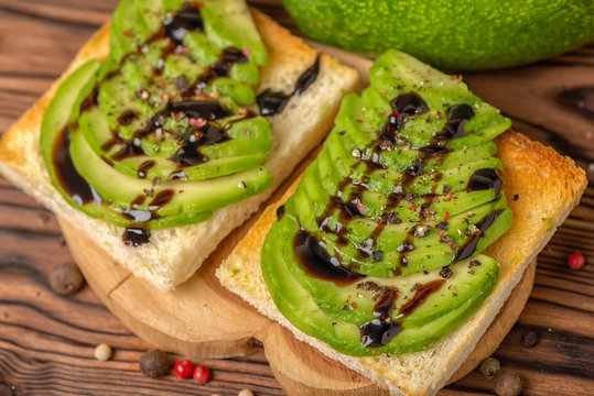 top view of sandwiches with sliced avocado, white bread toast decorated drizzled with sauce and sprinkle with pepper on wooden background, weight loss concept