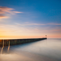Obraz premium Sunset on the beach with a wooden breakwater, long exposure