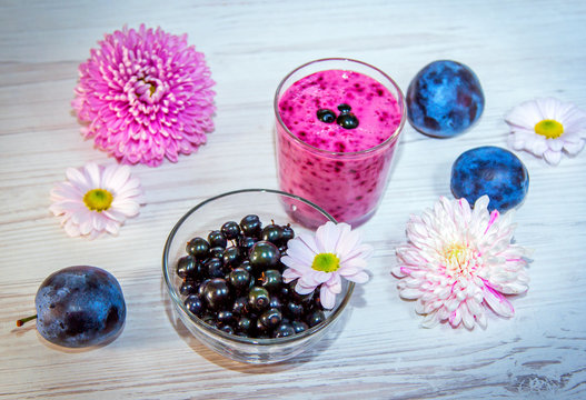 Fruit and berry smoothie in a glass, ripe plums, black currant and pink and white aster flowers on wooden background