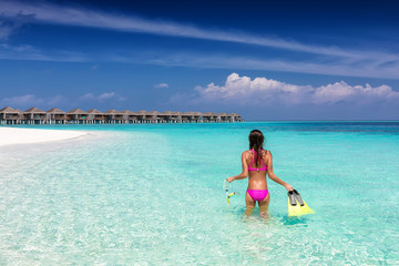 Fototapeta na wymiar Frau im Bikini und mit Schnorchelausrüstung steht am tropischen Strand der Malediven