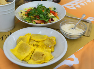 Ravioli stuffed with pumpkin (ravioli di zucca) served on white plate with italian-style salad and grated parmesan cheese in italian restaurant. Close-up.