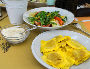Ravioli stuffed with pumpkin (ravioli di zucca) served on white plate with italian-style salad and grated parmesan cheese in italian restaurant. Close-up.