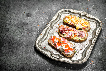 Various sandwiches with red caviar, bacon, cheese and fresh vegetables on a steel tray.
