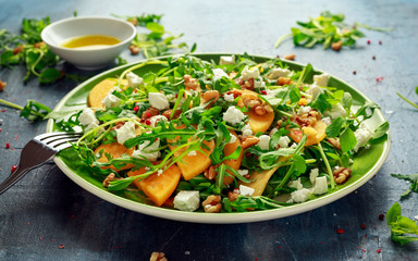 Fresh Tasty Persimmon salad with arugula, nuts, feta cheese, olive oil and herbs. healthy food