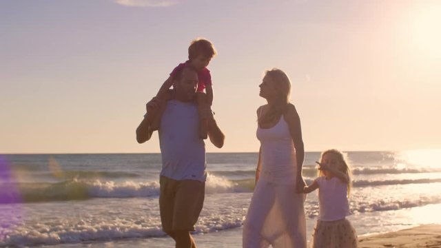 Young family walking and playing on beach parents carrying children on shoulders