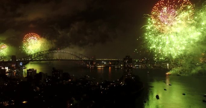 Up and back panning during New year 2018 fireworks in Sydney at night over city CBD landmarks reflecting in still waters of Harbour.
