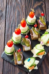 Tuinposter Canape with royal prawns, raw feta and herring on black bread on a slate board. Valentine's Day or wedding. © elena_hramowa