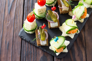 Canape with royal prawns, raw feta and herring on black bread on a slate board. Valentine's Day or wedding.
