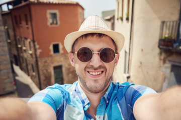 Smiling traveler in sunhat is making a selfie in a town street.