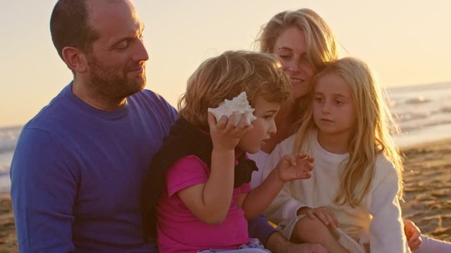 Young family sitting together on beach playing with sea shell