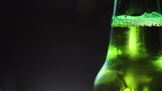 Drop of condensate drains on a green bottle of beer.