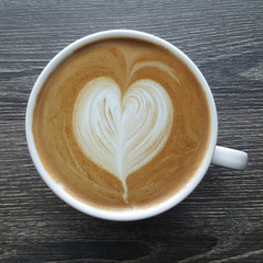 Top view of a mug of latte art coffee on timber background.