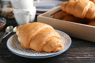 Plate with fresh yummy croissant on wooden table