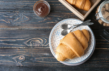 Plate with fresh yummy croissant on wooden table