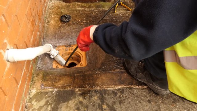 Professional plumber wearing safety vest and shoes is cleaning household sewage pipe outside the house