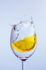 A slice of lemon falls into the glass with vodka. Bubbles and splashes appear