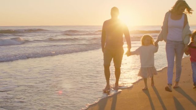 Young family walking and playing on beach with children holding hands in sunset