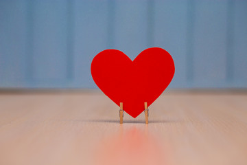 Red paper Heart of love with wooden clips on table with blue wooden background. Romantic symbol....