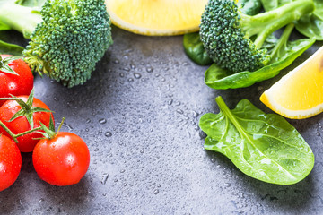 Spinach leaves, broccoli and slices of lemon fresh ingredients on grey stone background text space.