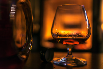 Time to enjoy! A glass filled with cognac stands on a table next to a cognac bottle. In the...