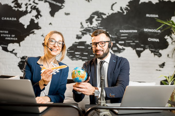 Couple of travel managers playing with globe and airplane sitting at the agency office with world map on the background