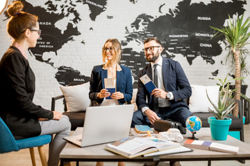 Young businesscouple choosing a trip with agent sitting at the travel agency office with world map...