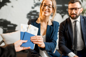 Young businesscouple choosing a trip with agent sitting at the travel agency office with world map...