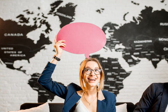 Young woman manager dreaming with colorful bubble above the head sitting at the office with world map on the background